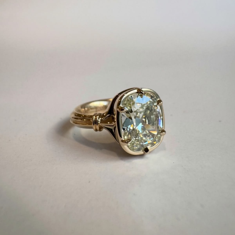 Gold cushion cut diamond engagement ring in collet setting.