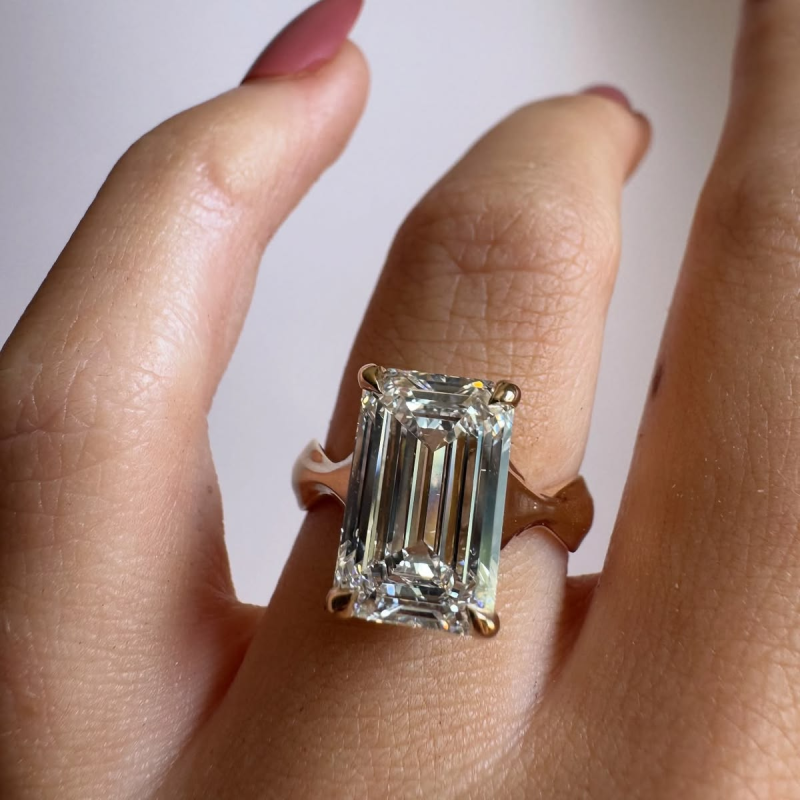 Solitaire emerald cut diamond engagement ring with unique curved band.